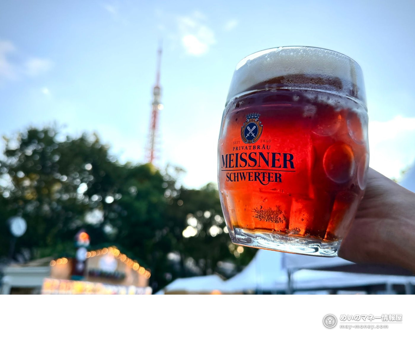 以东京塔为背景举起一杯红褐色啤酒，杯上写着 MEISSNER SCHWERTER