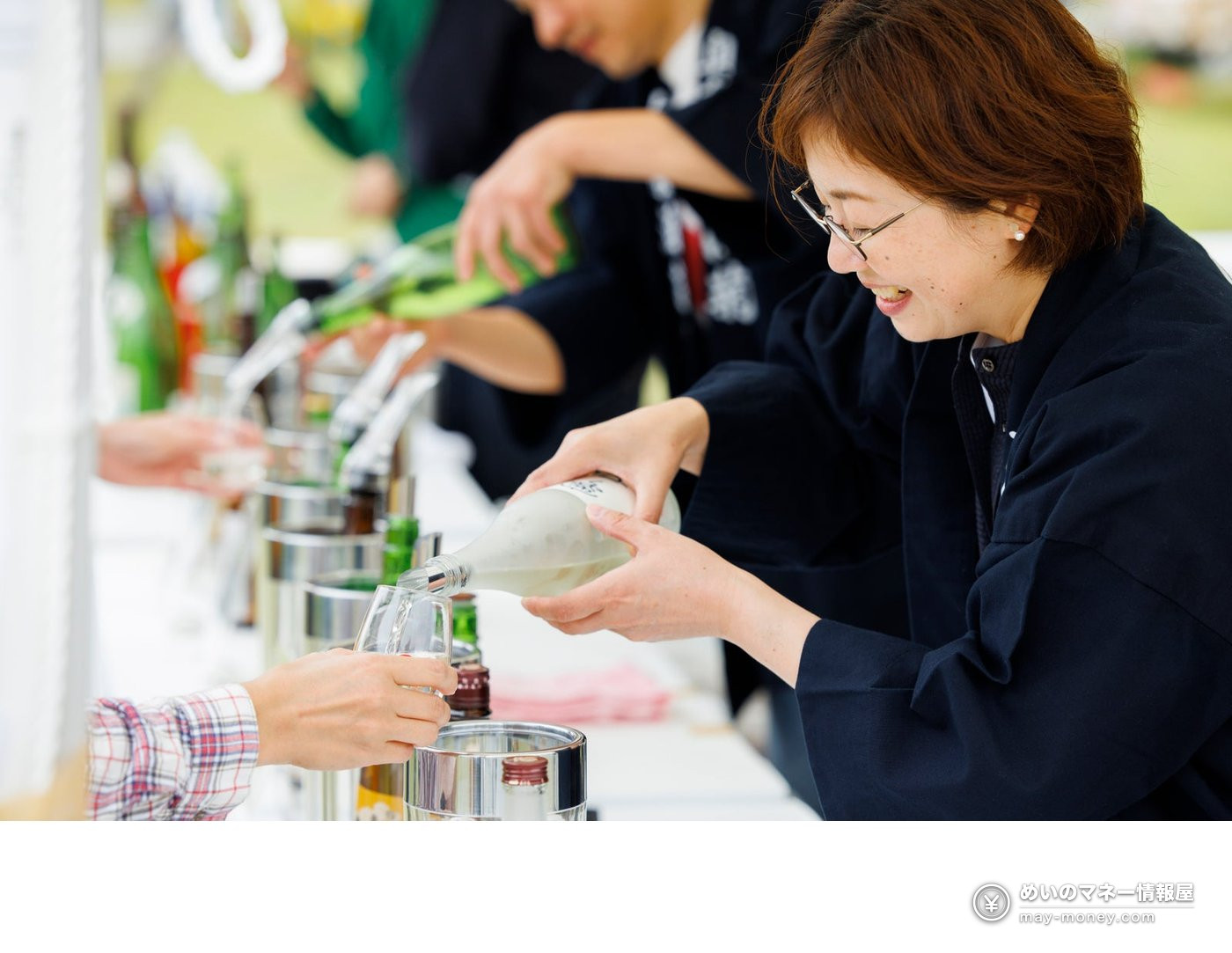 A woman in a happi coat pouring sake into a visitor's glass