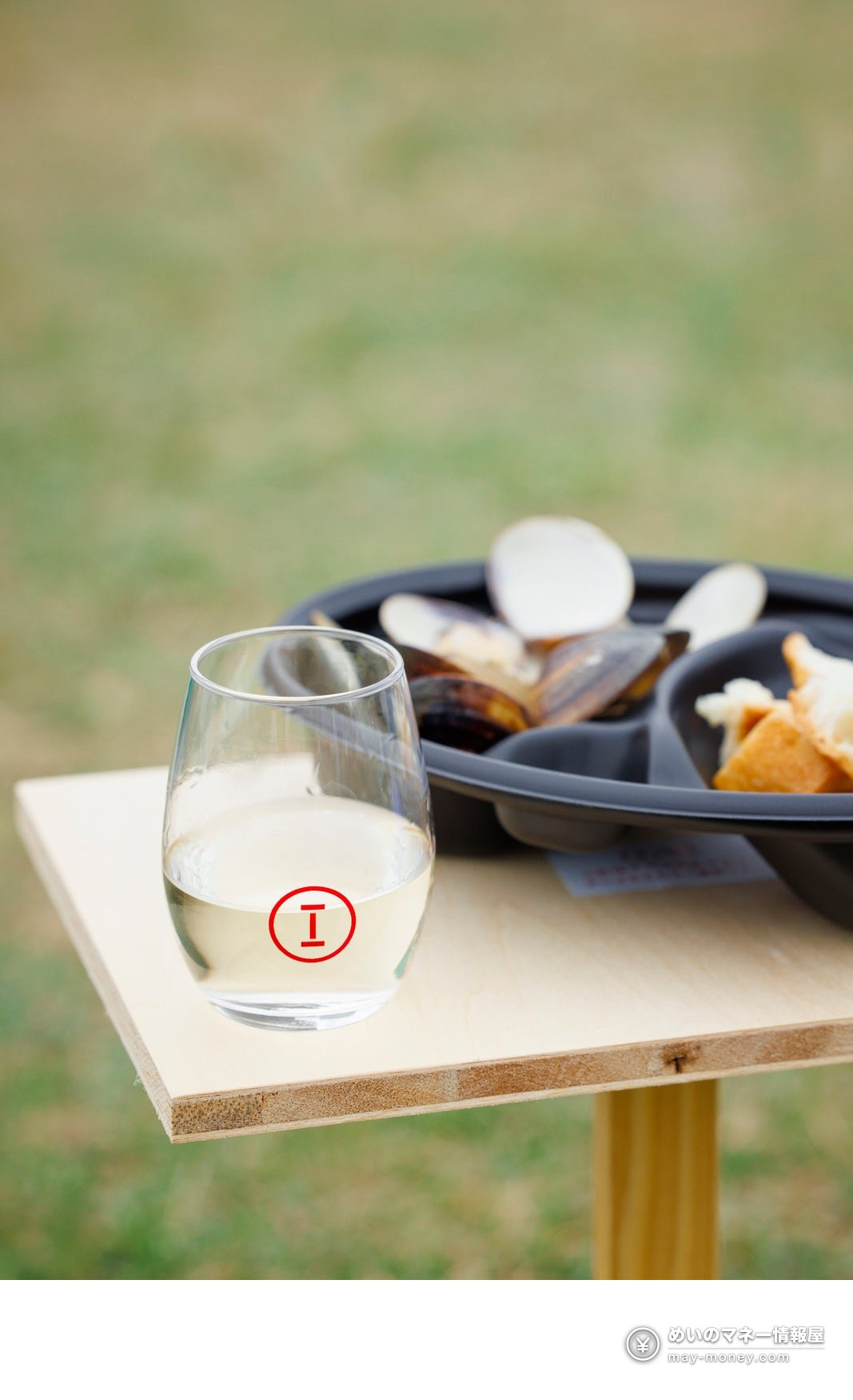 A Sake Marche glass and a plate of shellfish on an outdoor wooden table