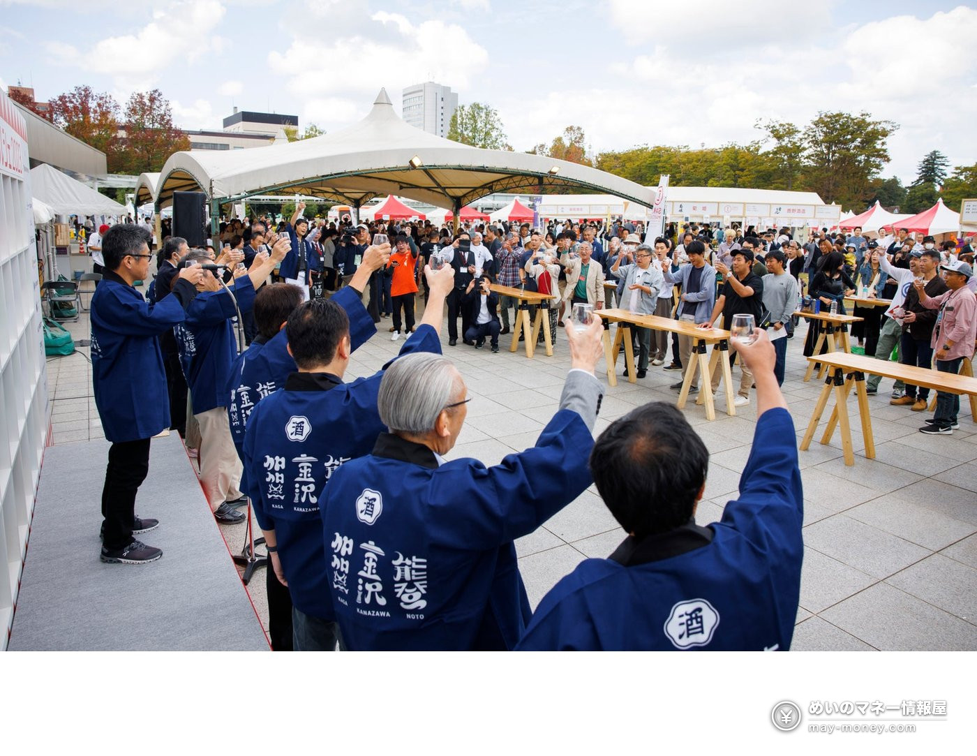 People in blue happi coats raising their glasses at the outdoor festival