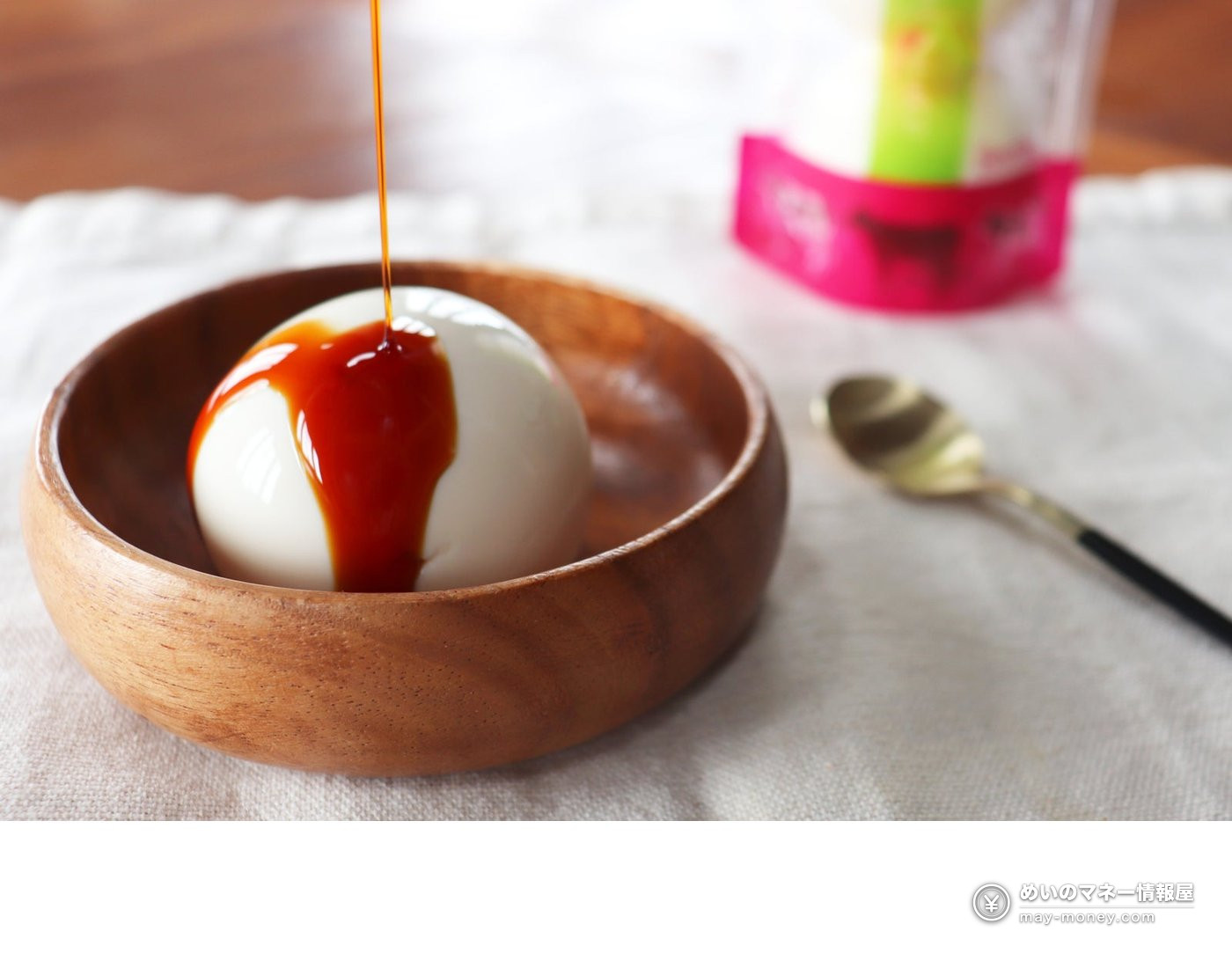 A round white dessert in a wooden bowl with brown sauce being poured over it
