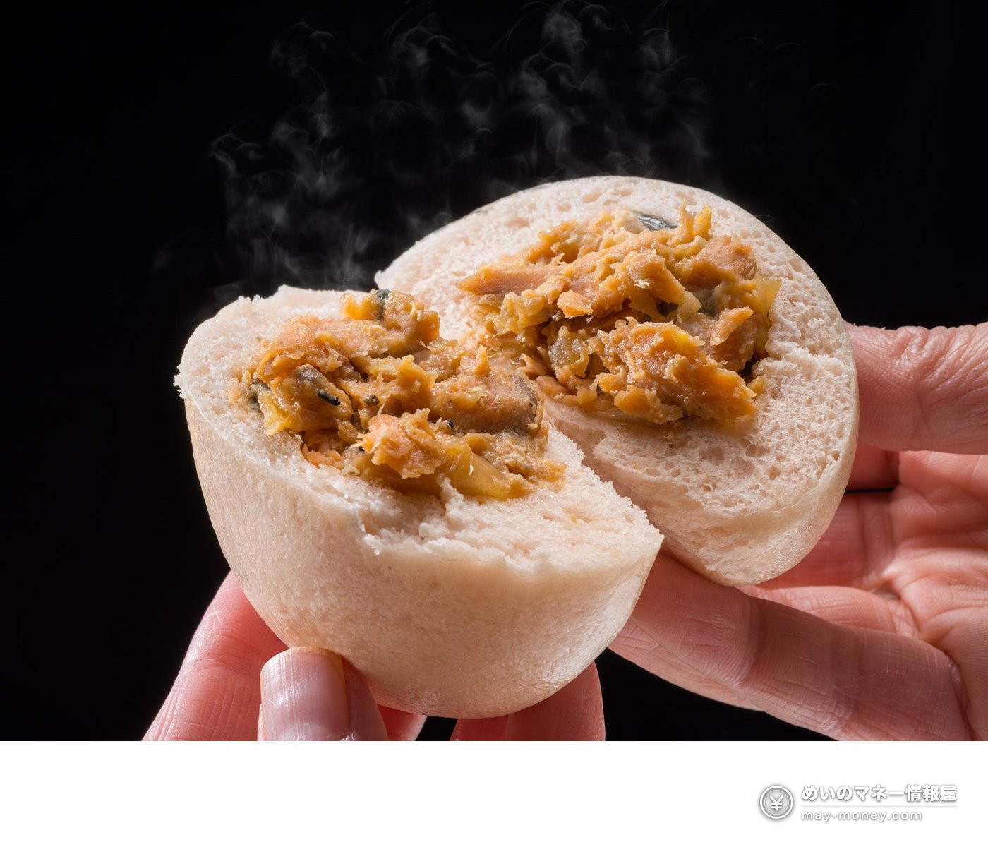 Hands splitting a steaming bun in half to show the filling