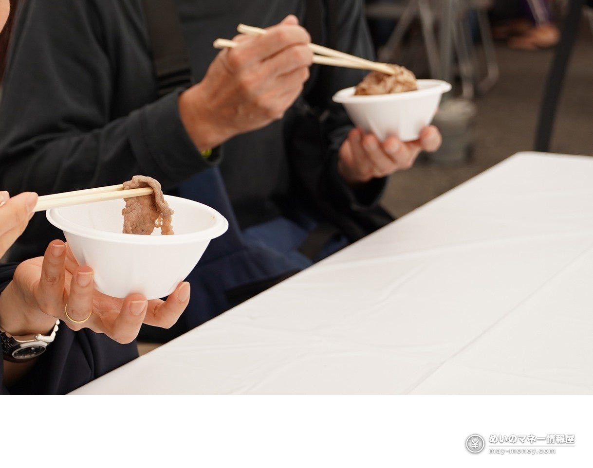 来场者用筷子夹起纸盘中的肉类料理（2025年试吃情景）
