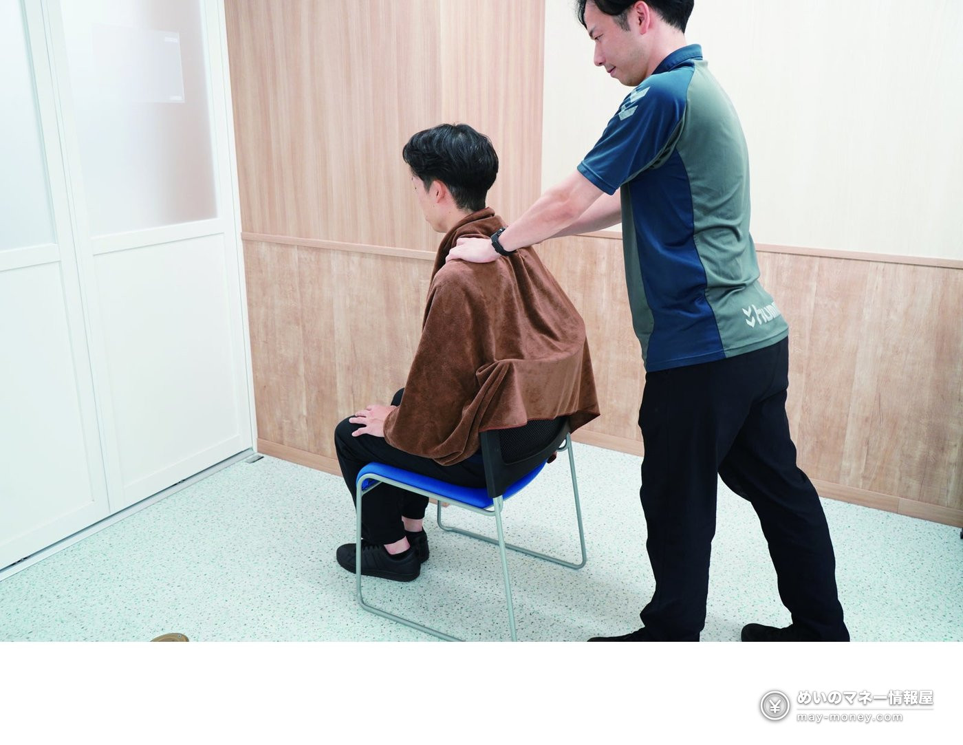 椅子に座った人の肩に、布の上から手を当てる男性