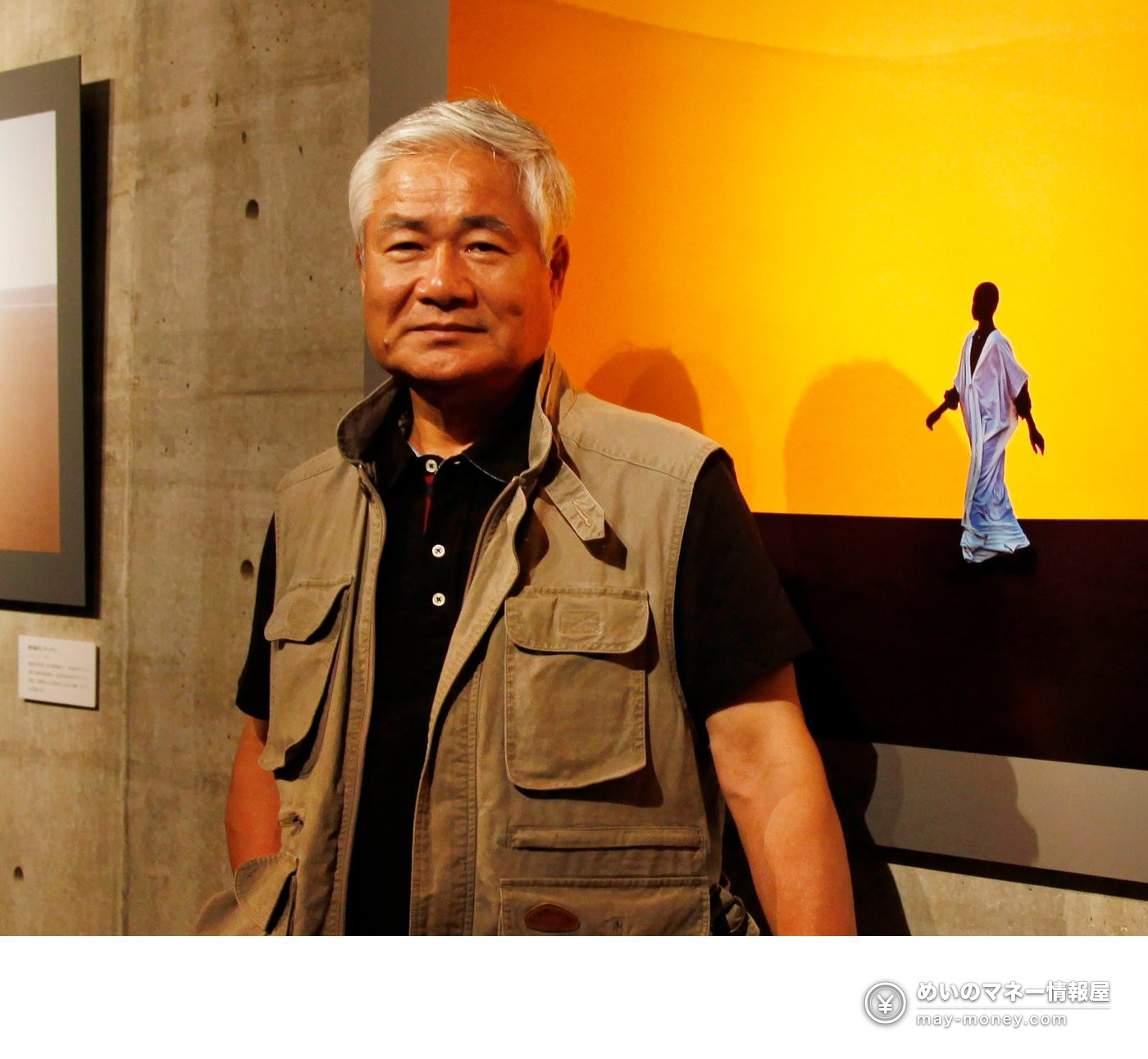 展示された写真の前に立つ、白髪でベスト姿の男性