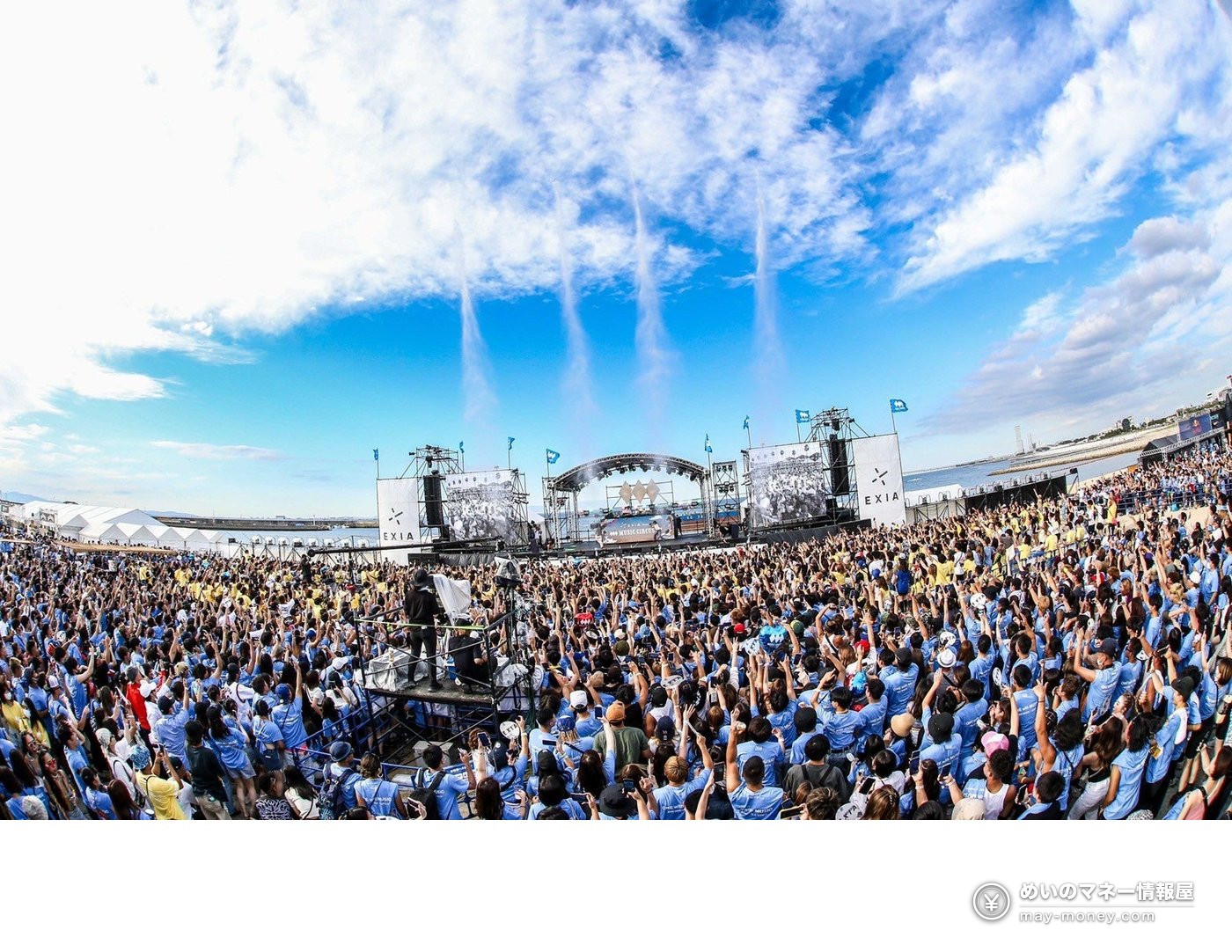 青空の下、水色のTシャツを着た大観衆が集まる野外ライブ会場
