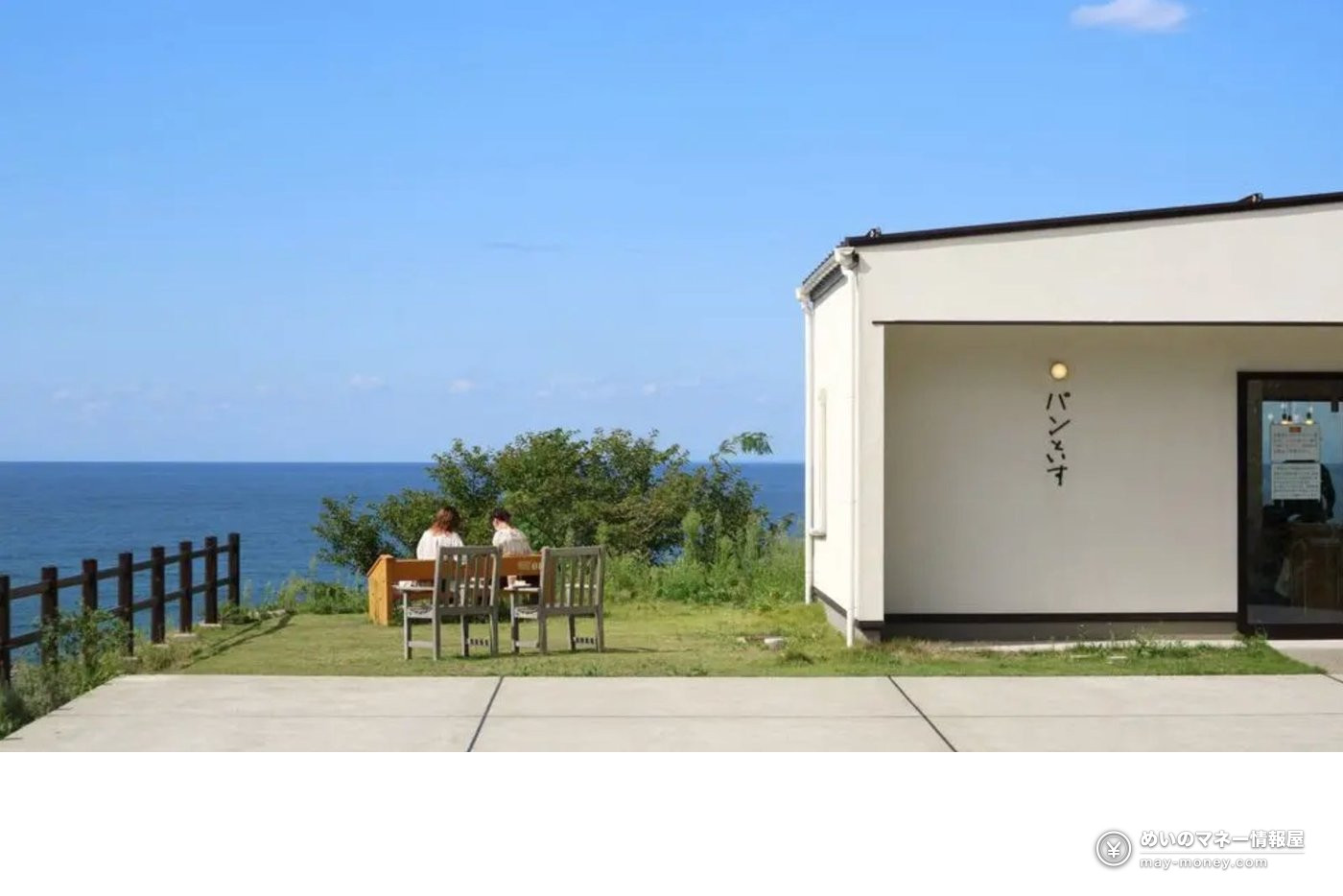 Two people on a lawn looking at the sea beside a white seaside building