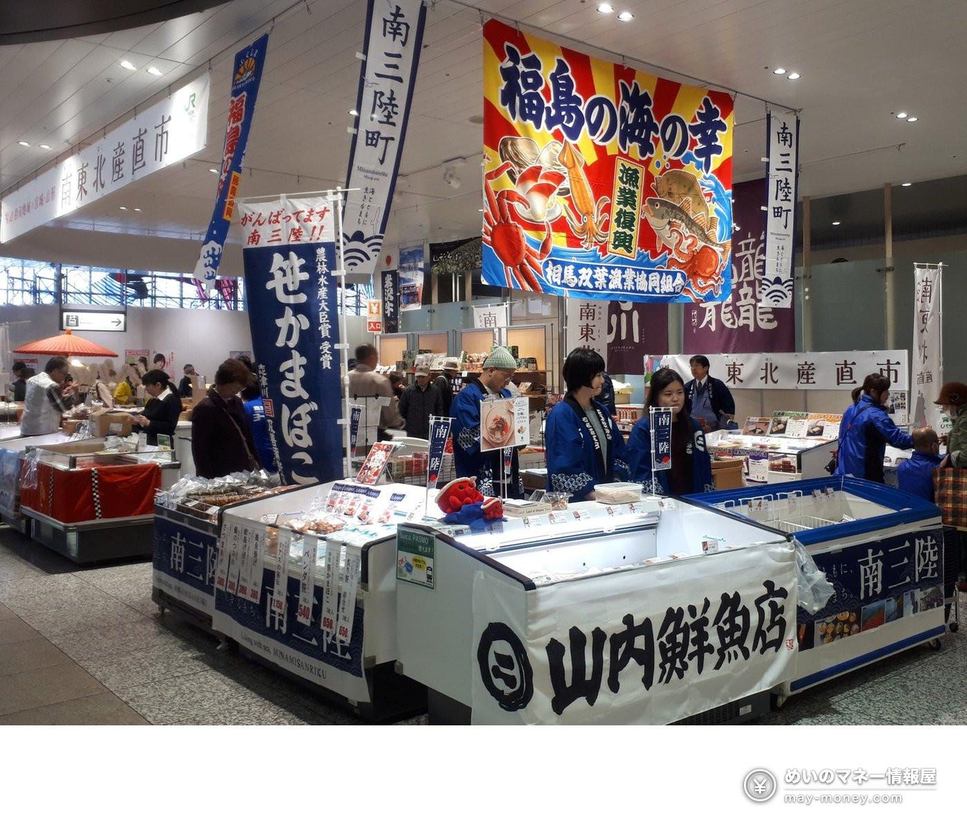 Minamisanriku Food Fair at Omiya Station: Seafood, Sweets and Wine, Nov 27–29 1 A station-concourse market stall where staff in happi coats sell fresh fish and fish cakes under Minamisanriku signs