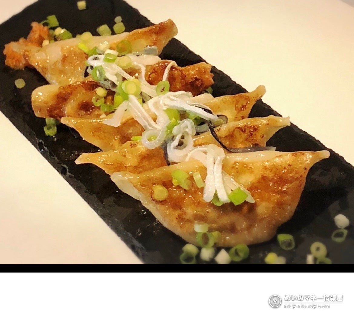 Pan-fried gyoza topped with shredded white leek and green onion on a black plate