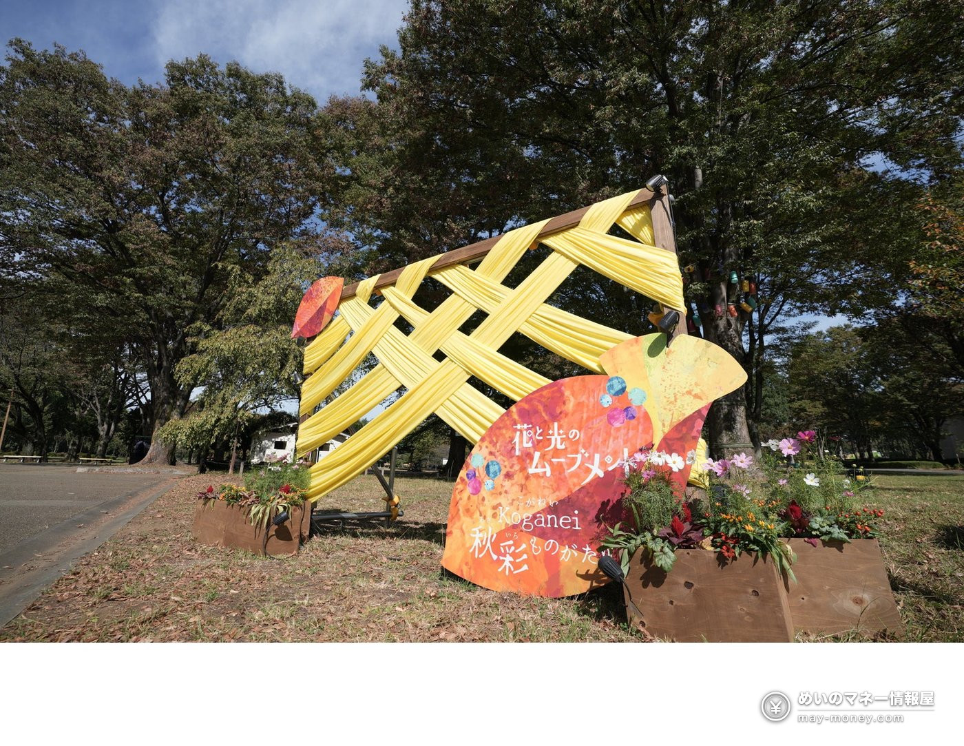 Wooden frame woven with yellow fabric next to a leaf-shaped sign and flowerbed