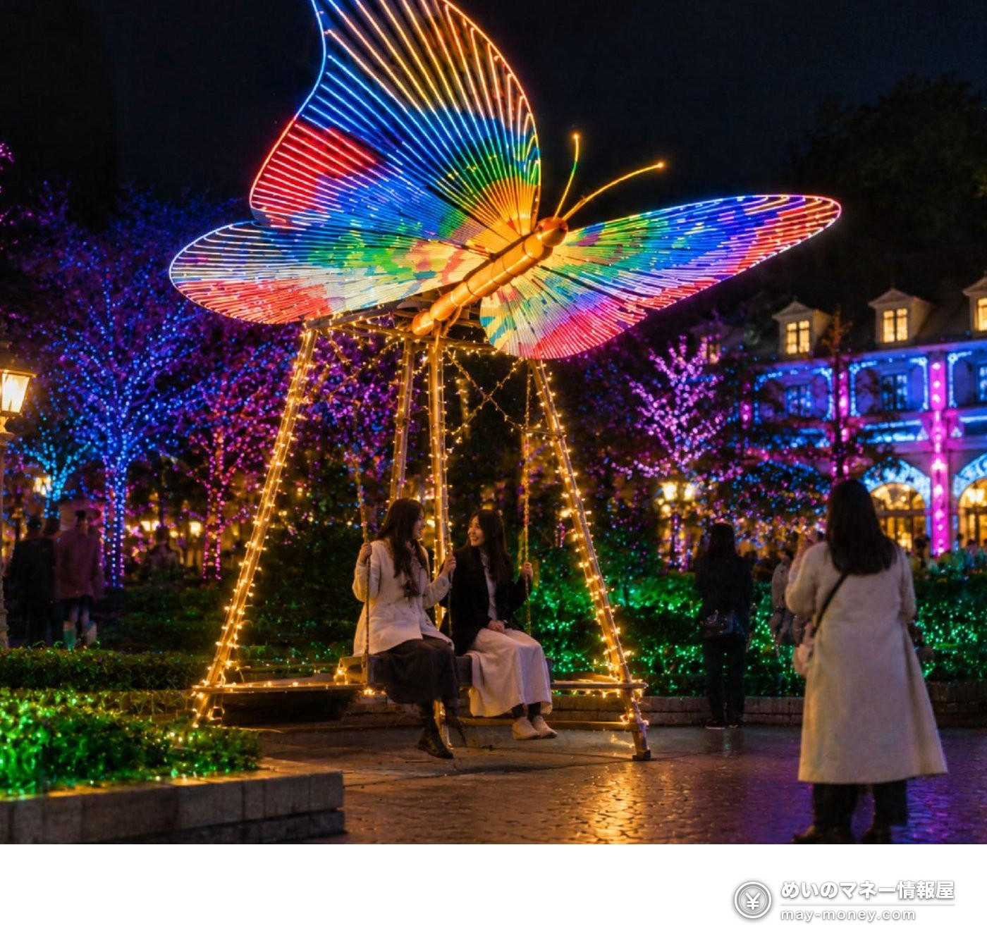 Two women sitting on a giant rainbow-colored butterfly swing at Kobe Illuminage