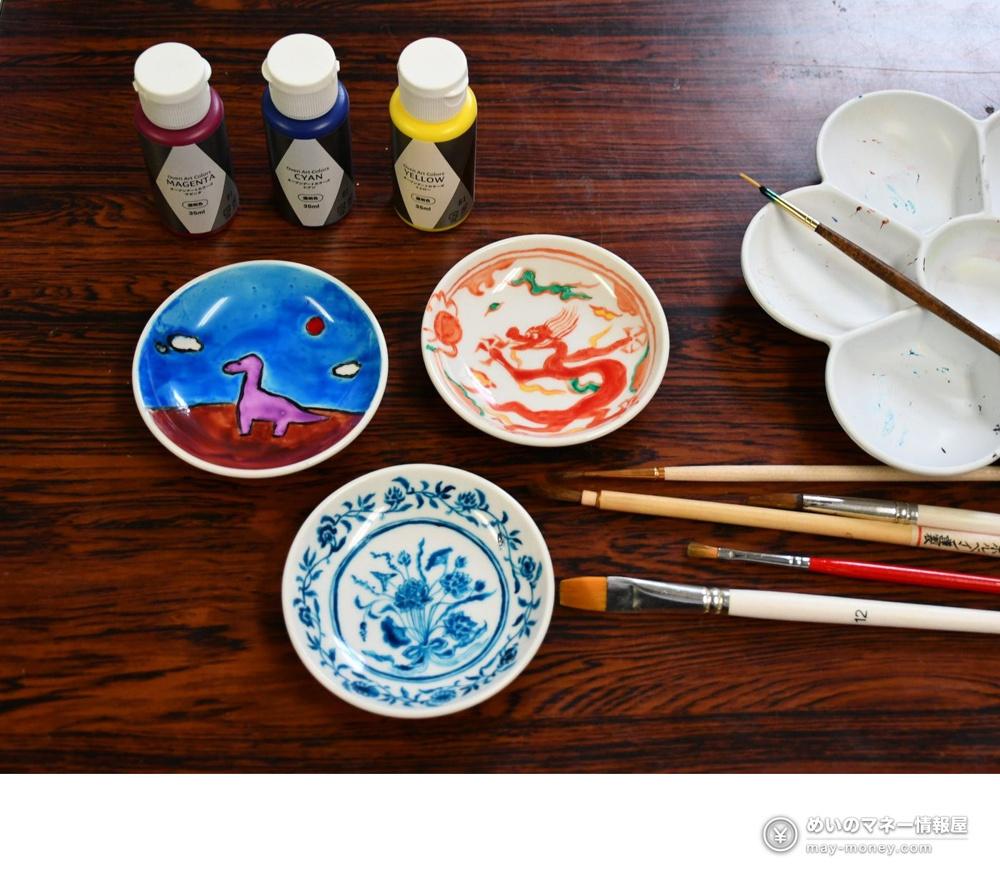 Three hand-painted small dishes with paints, brushes and a palette on a table