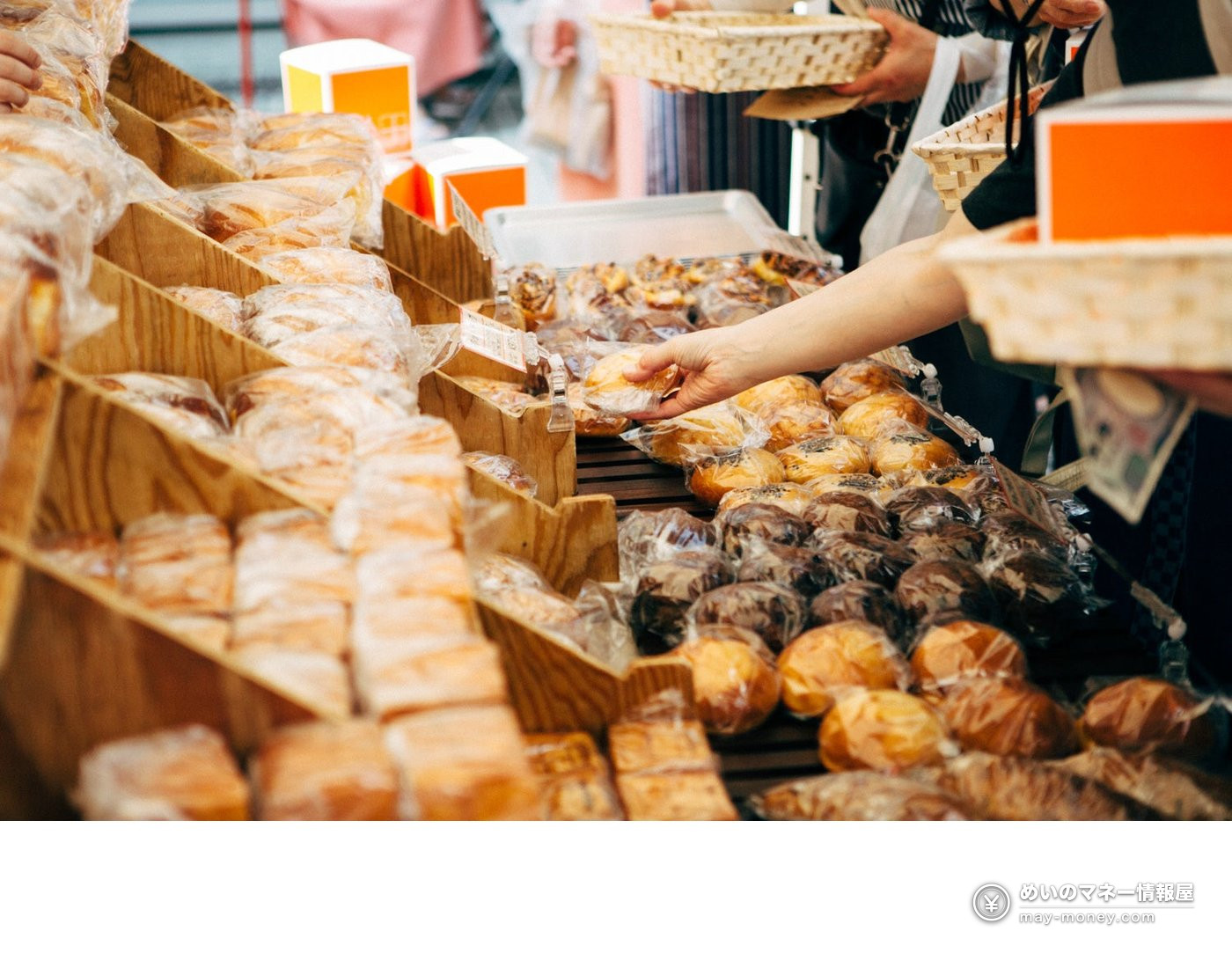 A shopper picking up bagged bread from a wooden market stall
