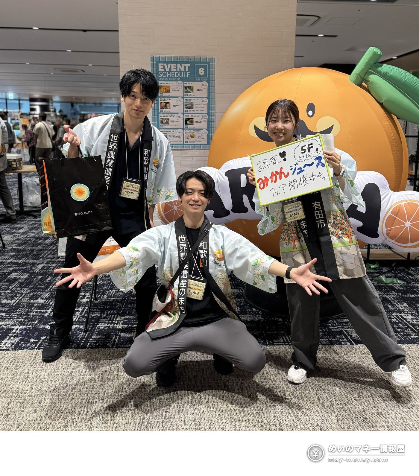 Three staff members in happi coats next to a giant mikan balloon at the Certified Mikan Juice Fair