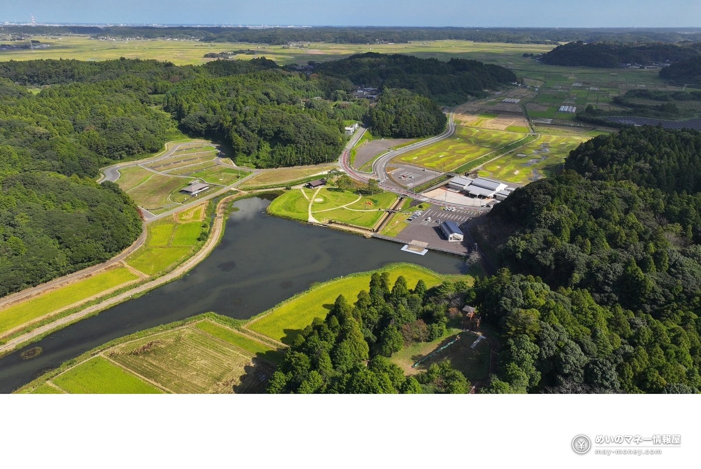Aerial view of a pond and park facilities surrounded by forest and rice fields