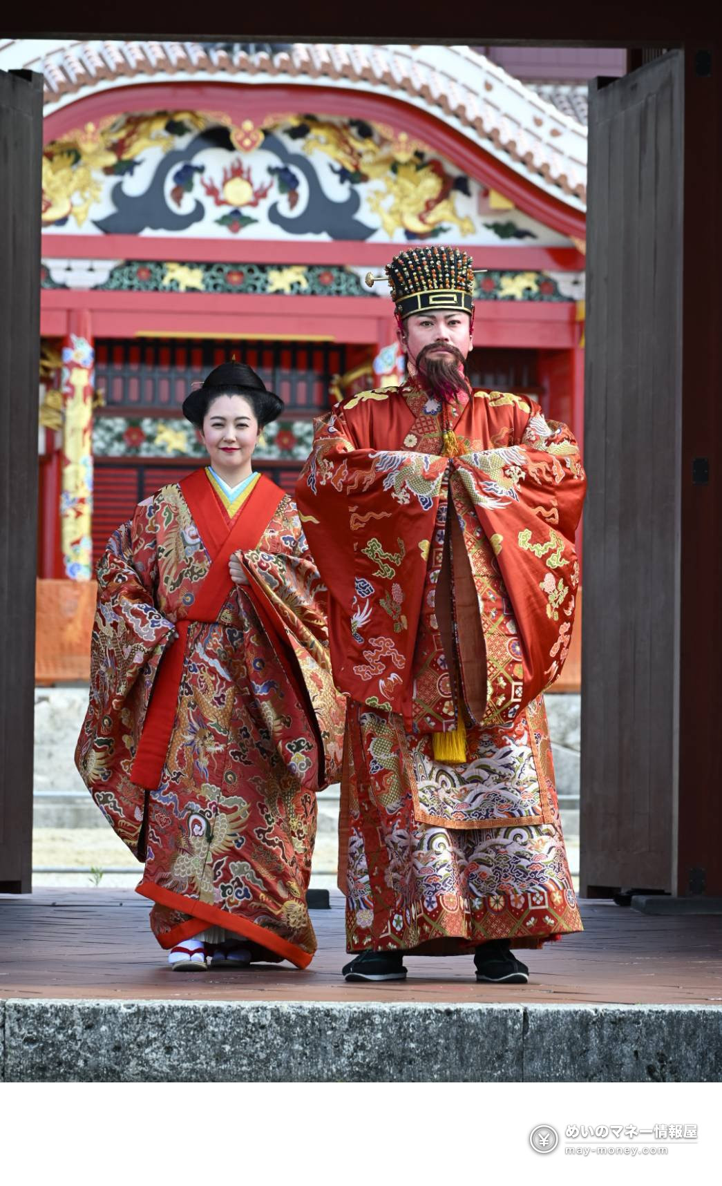 龍柄の赤い王族衣装をまとい、朱塗りの門の前に立つ男女