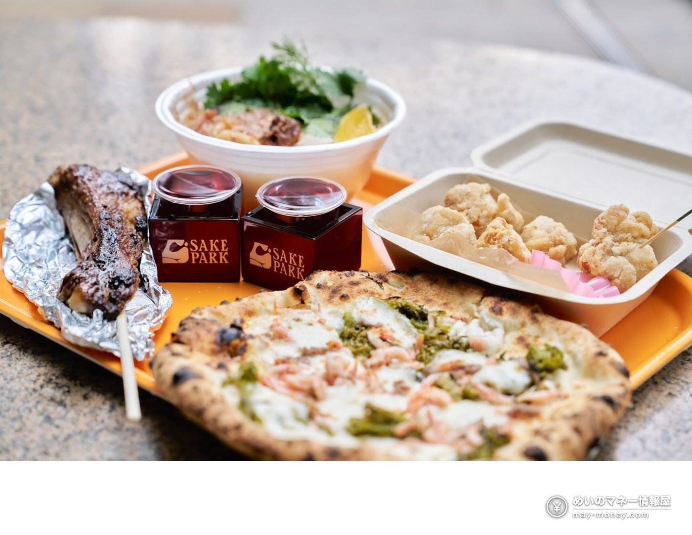 A tray with pizza, fried chicken, skewers and sake in a red masu cup at SAKE PARK