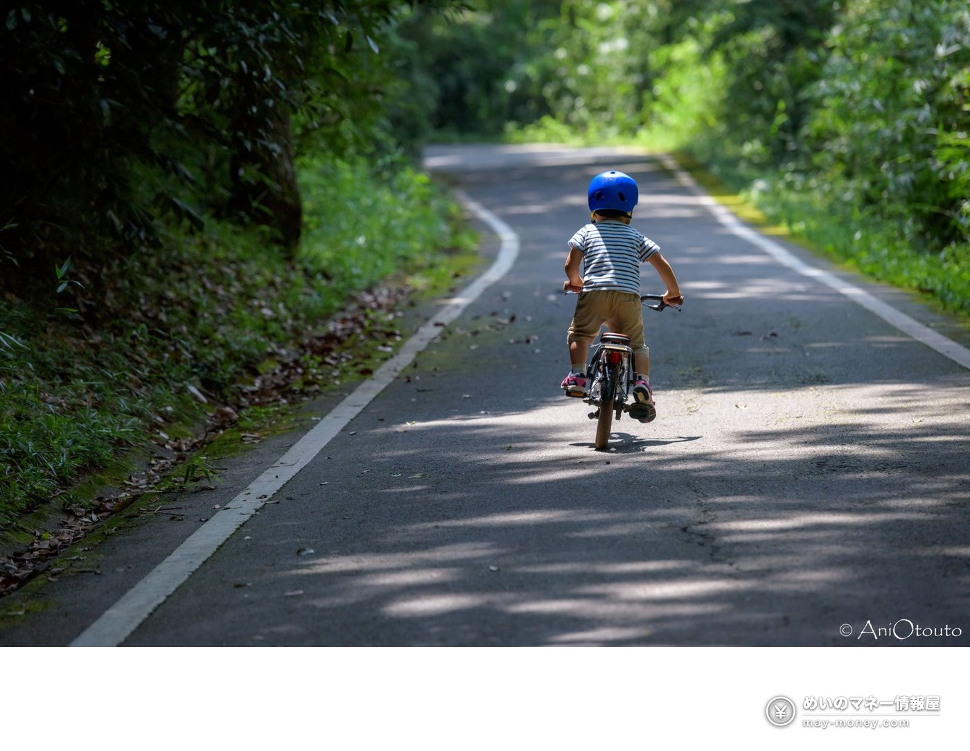 A child in a helmet cycling along a shaded paved path