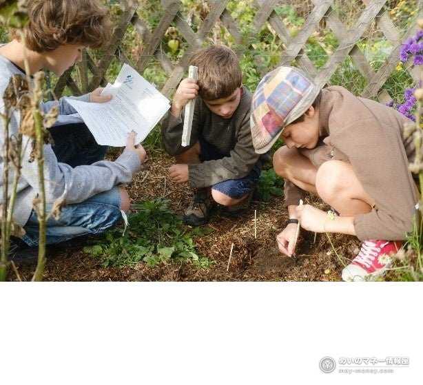 Three children examining the ground in a garden and reading a sheet of paper