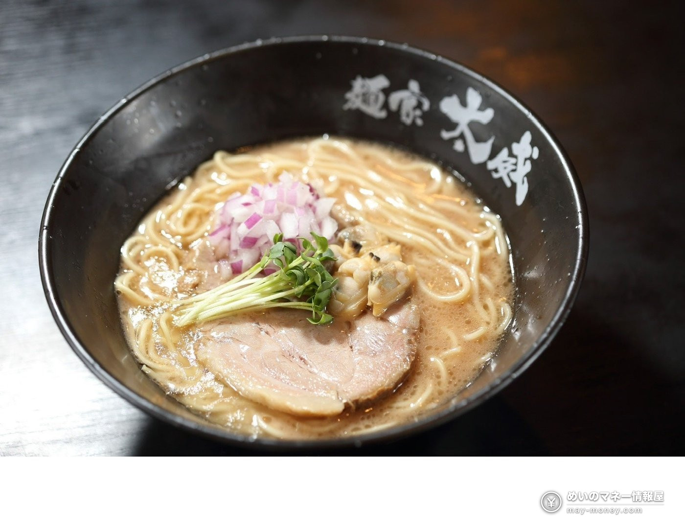 Ramen in a black bowl topped with shellfish, red onion, chashu pork and radish sprouts