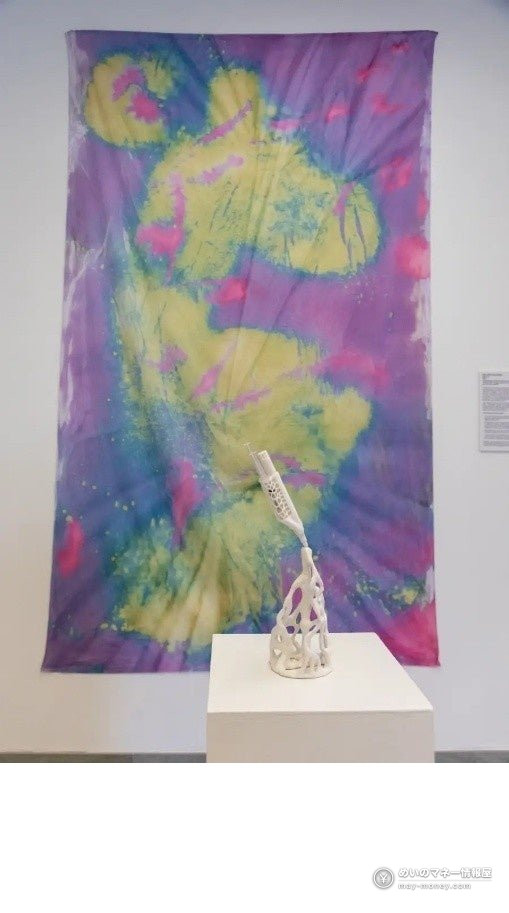 A white sculptural piece placed in front of purple and yellow dyed cloth