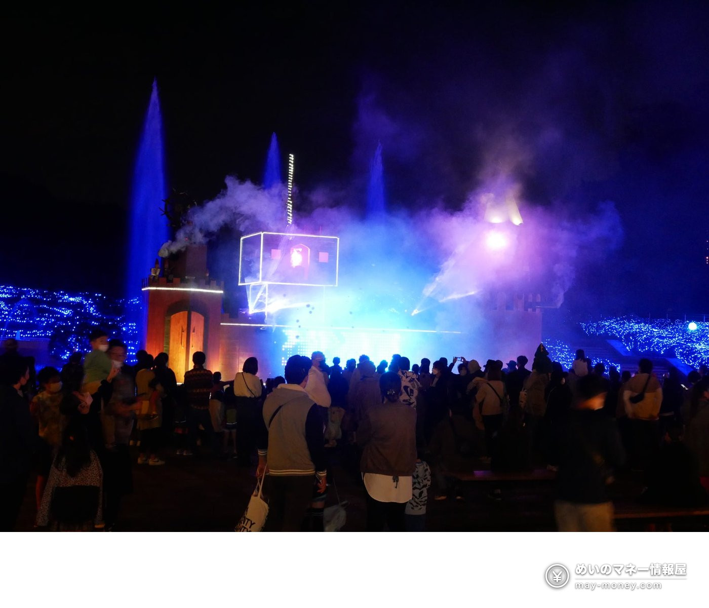 Visitors watching a light show at a castle-shaped stage set in a fountain at night