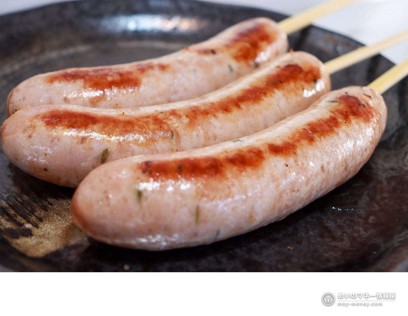 Three grilled sausage-style items on skewers on a black plate