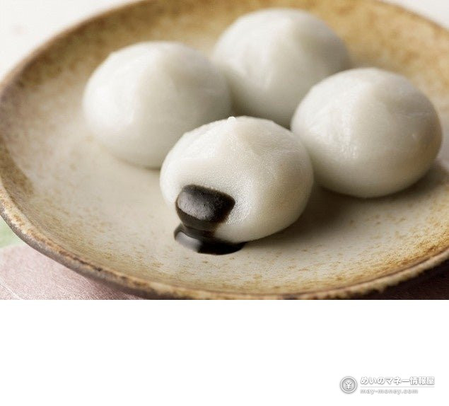 Four white rice dumplings on a plate, one showing a dark filling
