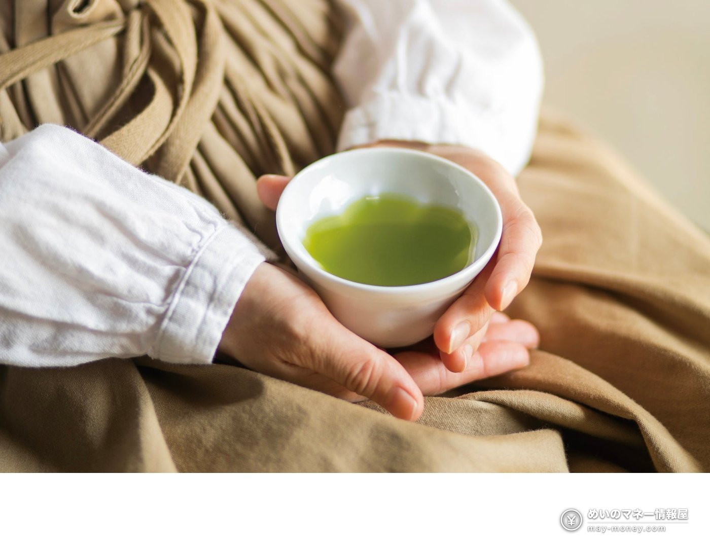 緑茶の入った白い湯呑みを両手で包む様子