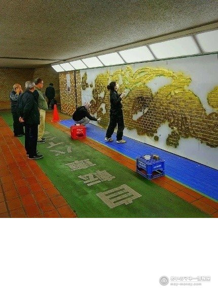A person painting a golden dragon on an underpass wall while others watch