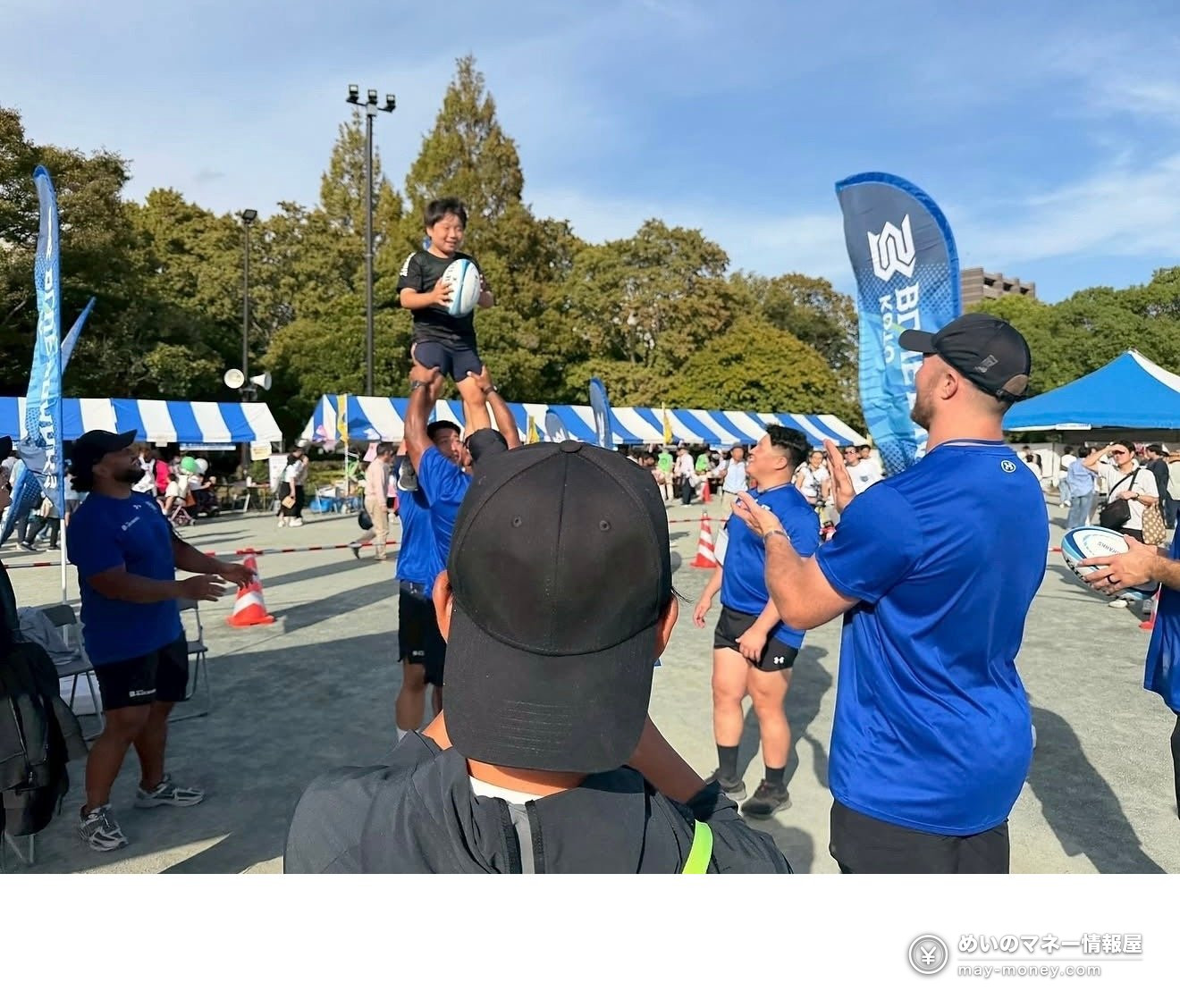 Players in blue shirts lifting a child holding a rugby ball outdoors