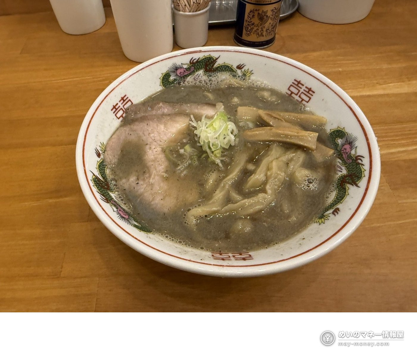 Bowl of ramen in a greyish broth topped with chashu pork and bamboo shoots, served in a dragon-pattern bowl